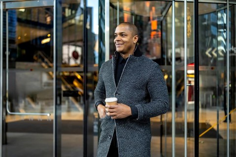 Confident young businessman standing outside a modern office building, holding a disposable coffee