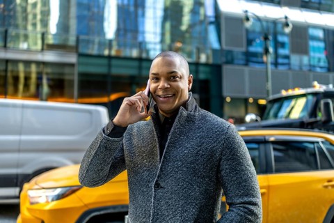 Smiling businessman making a phone call, standing on a busy street in manhattan with cars and