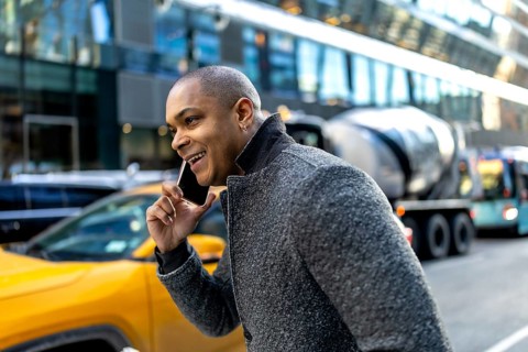 Smiling young executive talks on smartphone while walking a busy manhattan street, surrounded by