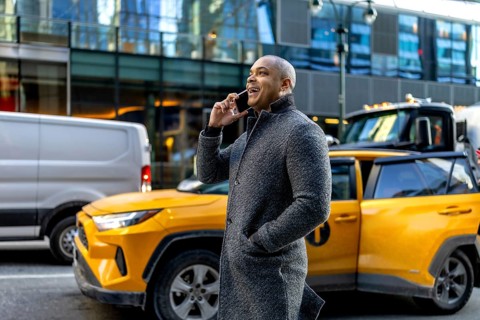 Happy professional businessman talking on a mobile phone, standing on a bustling urban street with