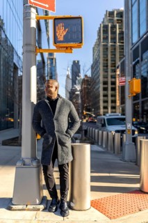 Smiling man standing on a manhattan street at a crosswalk with buildings and traffic in the