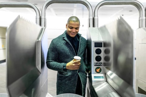Young professional passing a manhattan subway turnstile with a takeaway coffee, entering the metro