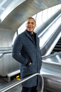 Young black businessman smiling and looking away while riding an escalator in a modern subway