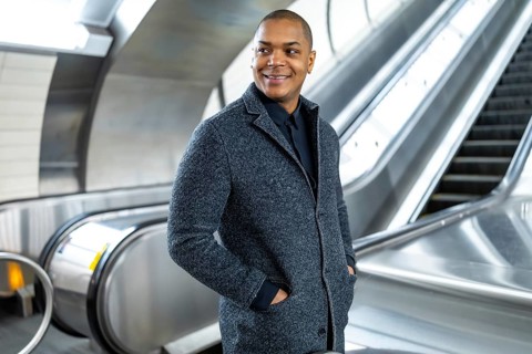 Professional black man smiling, standing confidently on an escalator in a modern subway station,