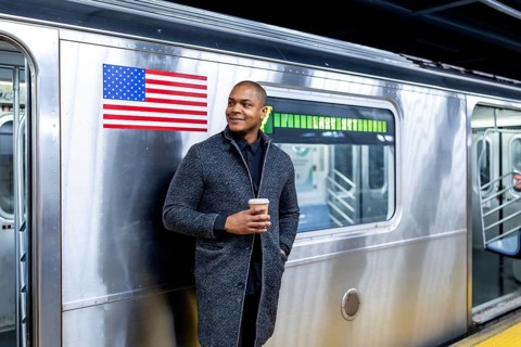 Smiling man standing on a subway platform in manhattan, enjoying a coffee while waiting for public