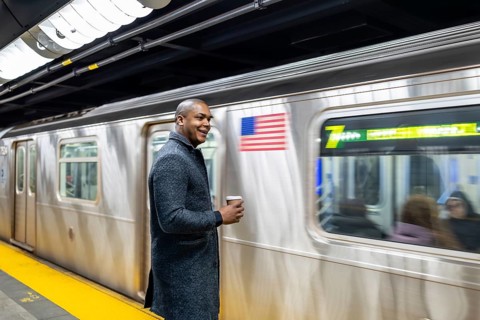 Young businessman standing on a brightly lit subway platform, happily waiting for his train while