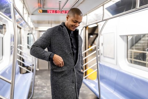 Young professional standing in a manhattan subway car, smiling as he adjusts his coat pocket, ready