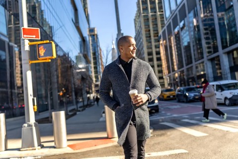 Young man in a stylish coat walks manhattan streets holding a coffee, confidently navigating