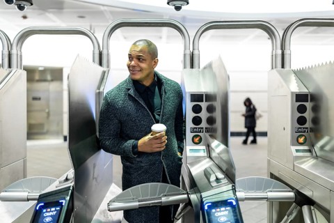 Professional man carrying a coffee cup, about to enter the subway system through modern turnstiles,