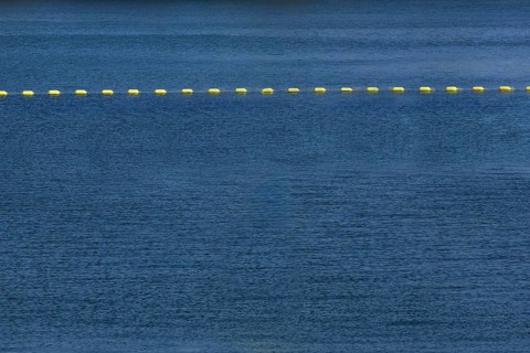 String of yellow cautionary navigation marker buoys on water surafce of river serving to warn,