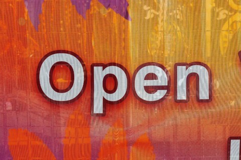 Close-up of the word open spelled out in white letters outlined in maroon color on textile banner,