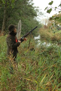 Female hunter with hunting rifle waits eagerly at the stream for flying ducks, Allgäu, Bavaria,