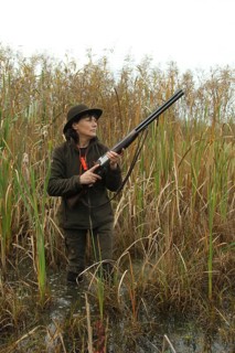 Female hunter standing in water with hunting rifle and eagerly waiting for flying ducks, Allgäu,