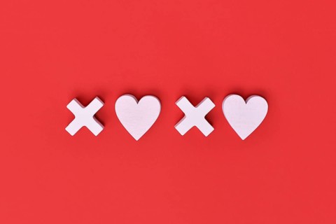 Valentine flat lay with wooden light pink hearts and XOXO letters arranged on a red background.
