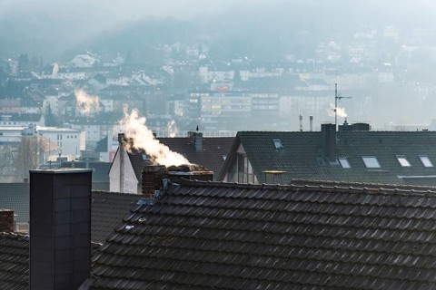 Smoke plume from a chimney over densely built residential area in the evening light, wintry city