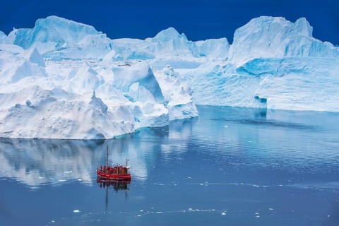 Aerial view of a tourist ship navigating through the fjord among icebergs calved from the
