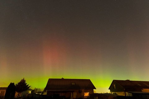 Shimmering red and green auroras over houses under clear starry skies, aurora borealis, Ilsede,