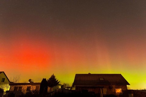 Red and green polar lights shine over houses, illuminated night sky, aurora borealis, Ilsede, Lower