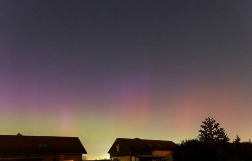 Shimmering purple and green auroras in the evening sky above residential buildings, aurora