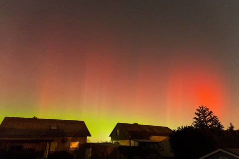 Red-green auroras illuminate the evening sky over residential buildings, aurora borealis, Ilsede,