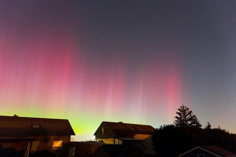 Intense red and green aurora glowing above the houses in the evening sky, aurora borealis, Ilsede,