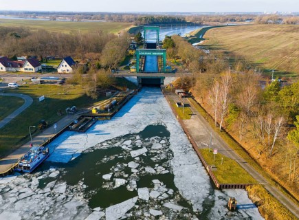 A frozen water surface in front of a lock, with gardens and trees on the edge, aerial view,