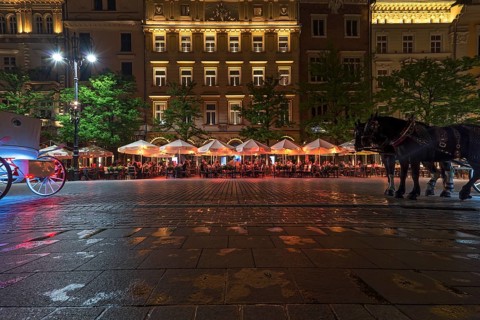 Restaurants on the market square at night, horse-drawn carriages left and right, Krakow, Poland