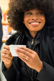 Smiling black woman holding a coffee cup, enjoying a warm drink in a new york city cafe, expressing