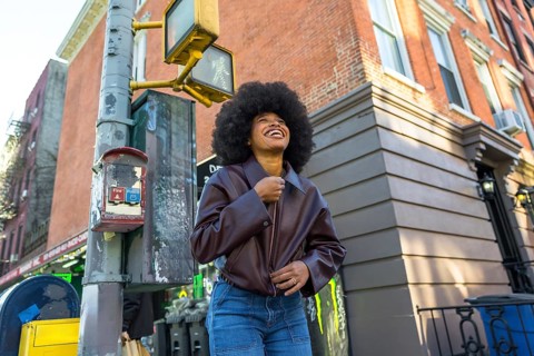 Young african american woman with afro hair smiling and looking up, walking in a vibrant new york