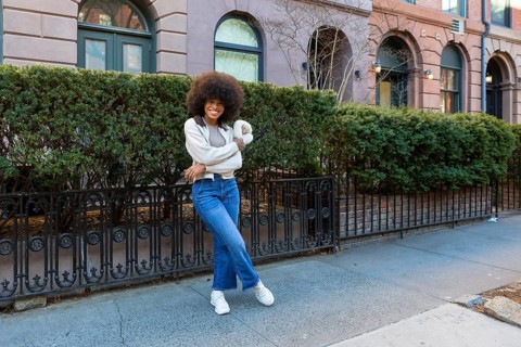 Young black woman with an afro hairstyle smiling confidently while standing on a sidewalk in front