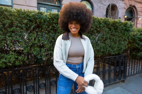 Joyful young black woman with a natural afro hairstyle walking and smiling confidently on a street