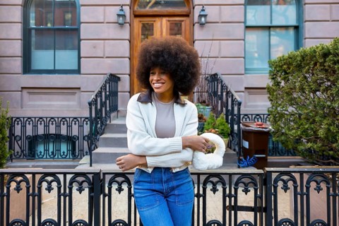 Smiling young woman with a large afro hairstyle and fashionable attire standing in front of a