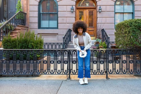 Smiling young black woman with afro hairstyle standing happily on a sidewalk in front of a classic