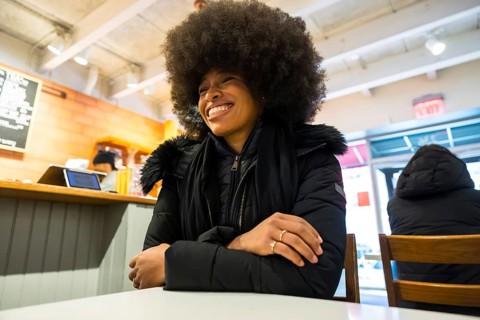 Smiling black woman in a winter jacket chatting happily inside a bustling manhattan coffee shop,
