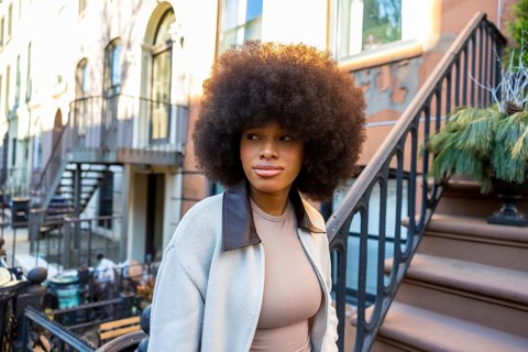 Young african american woman with voluminous afro hair standing on the steps of a brownstone