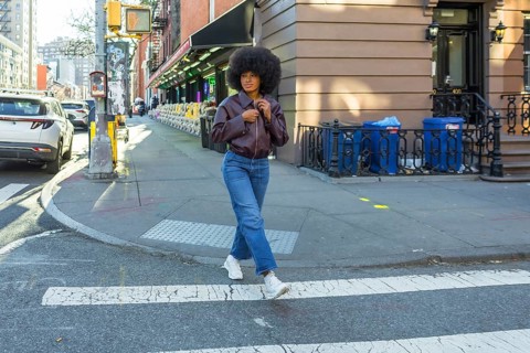 Young woman with afro hair and casual fashion attire confidently walking across a zebra crossing in
