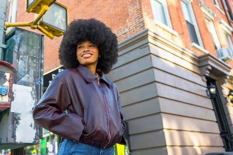 Young african american woman wearing a leather jacket and jeans, standing at a city intersection in