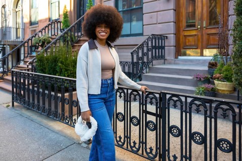 Young black woman with a large afro in jeans and a sweater, smiling confidently while standing on a