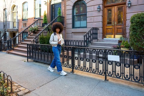 Young woman with afro hair walking down a sidewalk in a historical new york city neighborhood,
