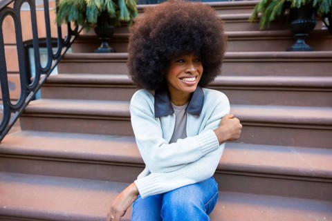Young black woman with an afro hairstyle smiling brightly while sitting on the brownstone steps of