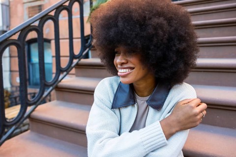 African american woman with a beautiful afro hairstyle sitting and smiling on brownstone steps in