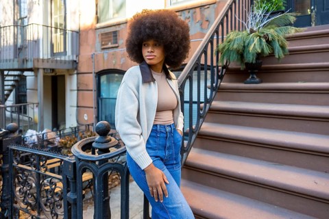 Stylish young woman with afro hair posing confidently on the brownstone steps of an urban building,