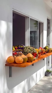 Assortment of fresh tropical fruit and young raw coconuts displayed on a wooden shelf outside a