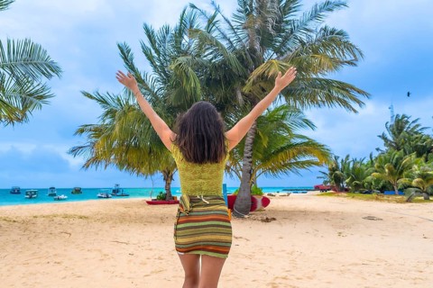 Woman standing on a white sand beach, raising arms to the sky, embracing joy and freedom during a