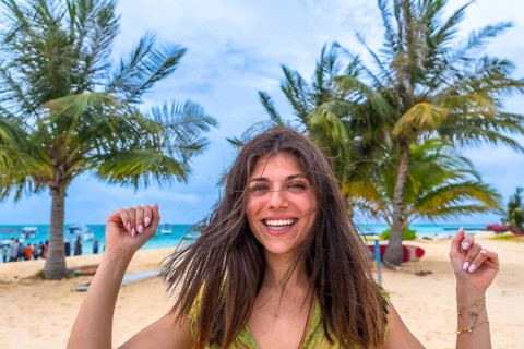 Young woman smiling with joy, celebrating her tropical beach vacation with swaying palm trees and