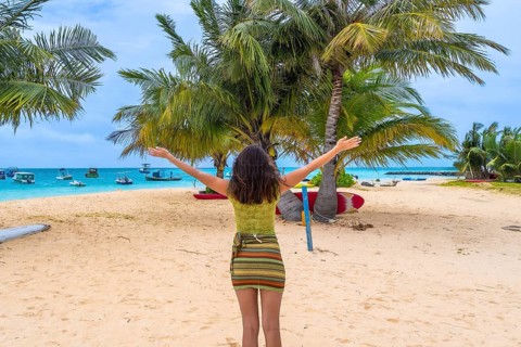 Woman standing on a tropical sandy beach with arms outstretched, experiencing a joyful moment of