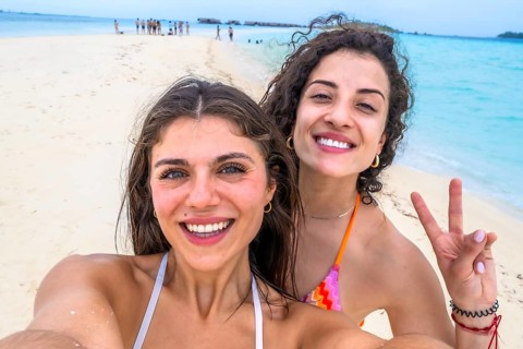Smiling women capturing a joyful selfie on a beautiful white sand beach with turquoise water during
