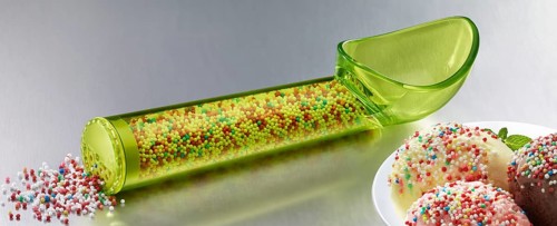 Yellow, transparent ice cream scoop filled with coloured sugar sprinkles, next to a plate with