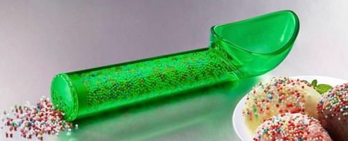 Green, transparent ice cream scoop filled with coloured sugar sprinkles, next to plates with