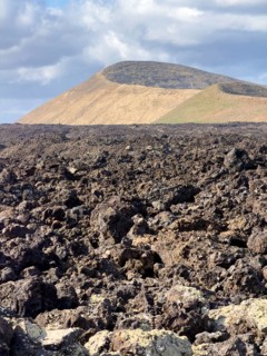 Hiking trail through lava rock to Caldera Blanca volcano against blue sky with white clouds, Mancha